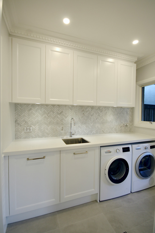 This is an example of a mid-sized single-wall dedicated laundry room in Sydney with an undermount sink, recessed-panel cabinets, white cabinets, quartz benchtops, grey splashback, marble splashback, white walls, a side-by-side washer and dryer, grey floor and white benchtop.