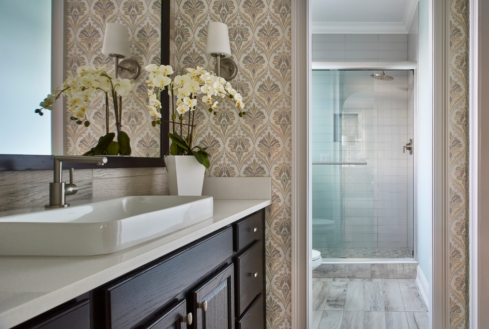Inspiration for a mid-sized transitional master bathroom in Austin with raised-panel cabinets, dark wood cabinets, an alcove shower, gray tile, ceramic tile, multi-coloured walls, light hardwood floors, a vessel sink and engineered quartz benchtops.