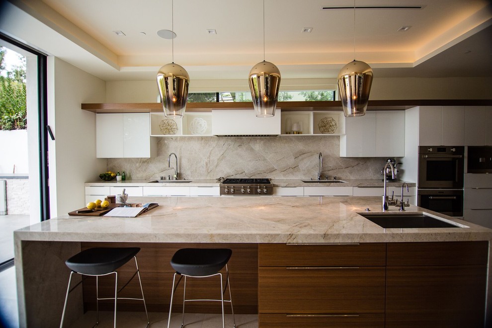 This is an example of a large contemporary galley kitchen in Los Angeles with an undermount sink, flat-panel cabinets, medium wood cabinets, quartzite benchtops, stone slab splashback, with island, beige splashback, stainless steel appliances and beige benchtop.