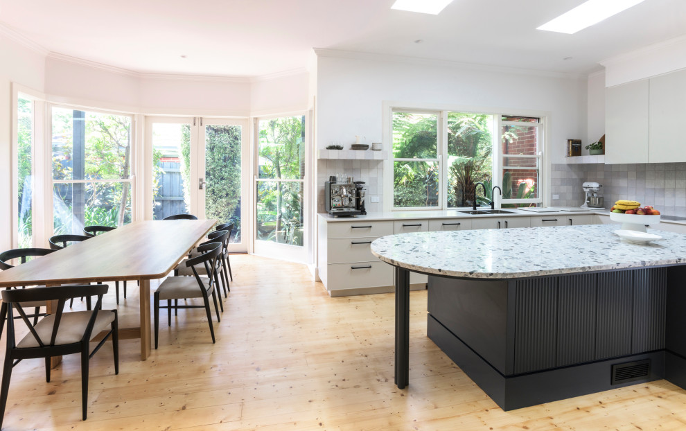 Photo of a large contemporary u-shaped open plan kitchen in Melbourne with a double-bowl sink, beige cabinets, terrazzo benchtops, black appliances, light hardwood floors and multi-coloured benchtop.