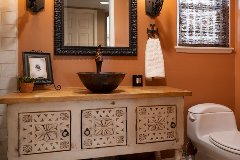 Пример оригинального дизайна: маленькая ванная комната в средиземноморском стиле с фасадами островного типа, белыми фасадами, душем в нише, унитазом-моноблоком, бежевой плиткой, керамогранитной плиткой, оранжевыми стенами, полом из винила, душевой кабиной, настольной раковиной, столешницей из дерева, бежевым полом, душем с распашными дверями, коричневой столешницей, тумбой под одну раковину и напольной тумбой для на участке и в саду