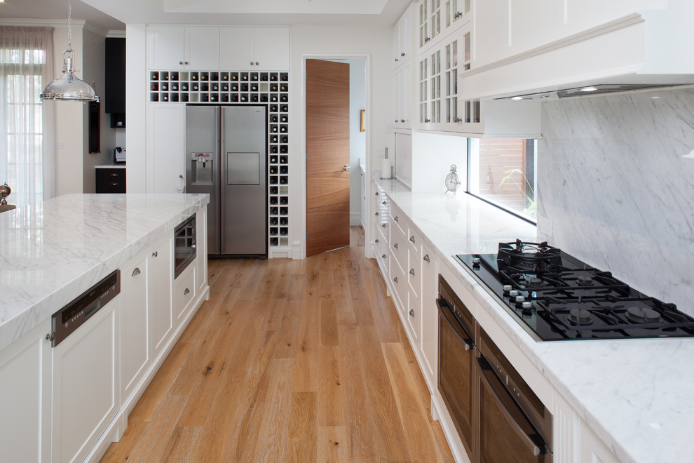 This is an example of a large traditional kitchen in Perth with recessed-panel cabinets, white cabinets, marble benchtops, stone slab splashback, stainless steel appliances, with island, grey splashback, grey benchtop and light hardwood floors.