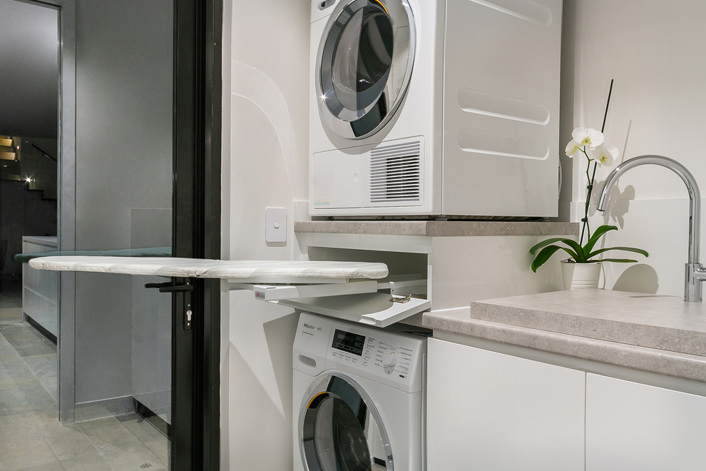 Photo of a modern single-wall dedicated laundry room in Perth with an undermount sink, beaded inset cabinets, white cabinets, laminate benchtops, white walls, marble floors, a stacked washer and dryer, grey floor and grey benchtop.