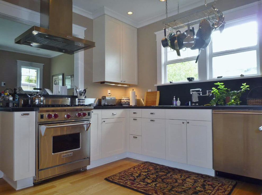 Small transitional u-shaped medium tone wood floor and brown floor enclosed kitchen photo in Seattle with a double-bowl sink, recessed-panel cabinets, white cabinets, stainless steel appliances and black countertops