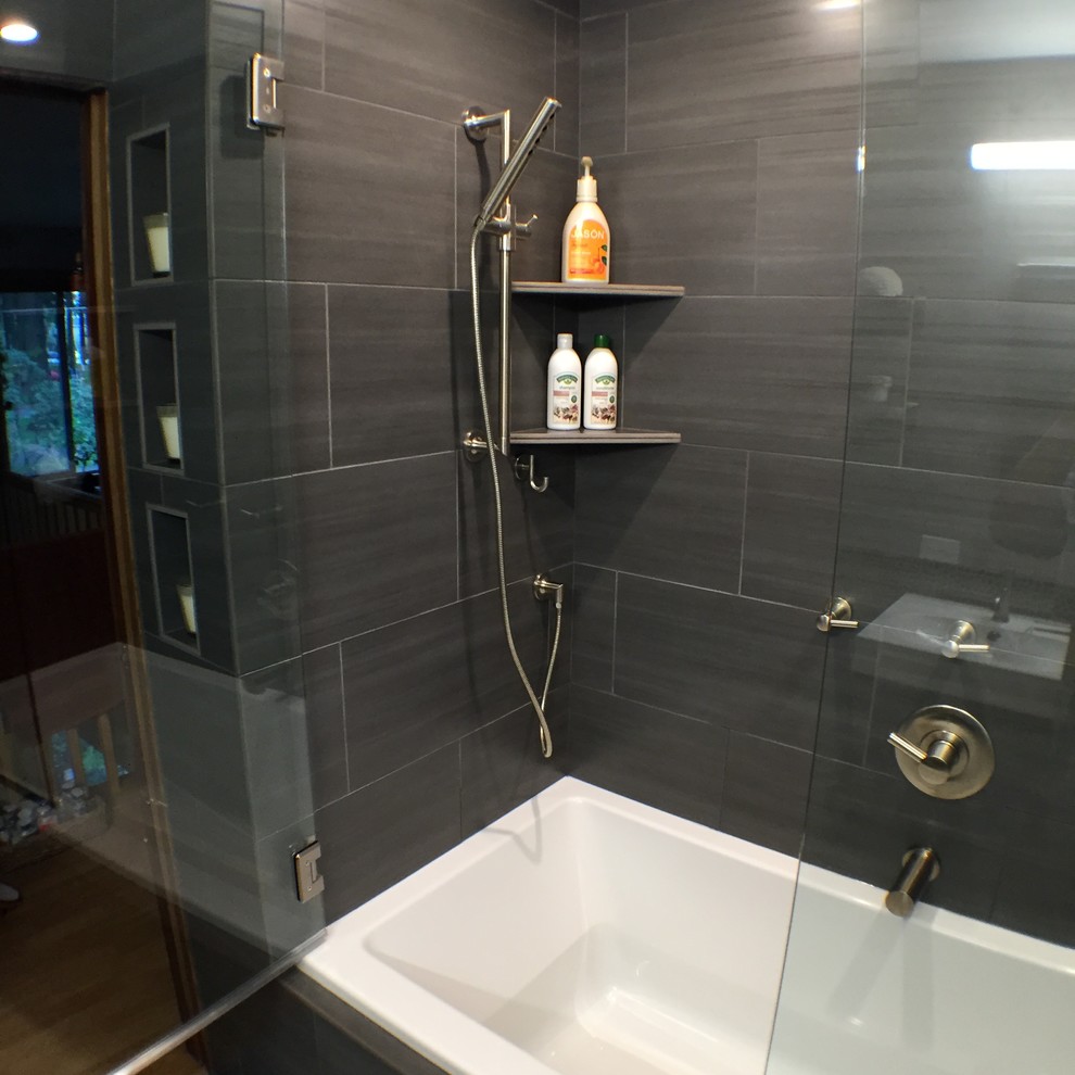 This is an example of a mid-sized contemporary master bathroom in Portland with a console sink, solid surface benchtops, an alcove tub, a shower/bathtub combo, a one-piece toilet, black tile, porcelain tile and black walls.