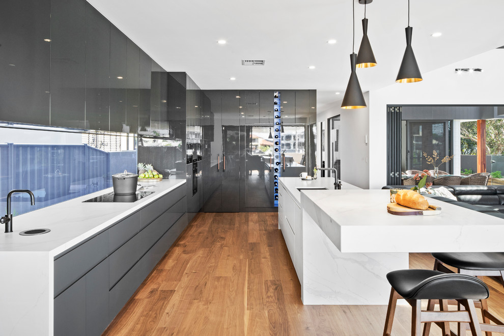 Design ideas for a contemporary l-shaped open plan kitchen in Sunshine Coast with an undermount sink, flat-panel cabinets, black cabinets, window splashback, panelled appliances, medium hardwood floors, with island, brown floor and white benchtop.