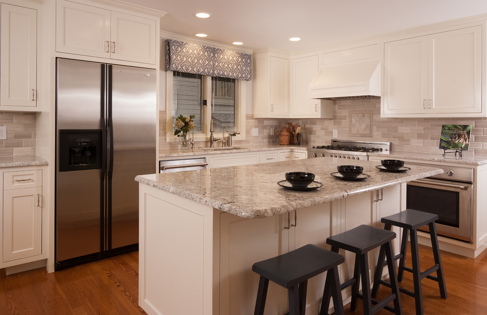 Example of a mid-sized transitional l-shaped medium tone wood floor and brown floor enclosed kitchen design with an undermount sink, recessed-panel cabinets, white cabinets, quartz countertops, gray backsplash, stone tile backsplash, stainless steel appliances, an island and gray countertops