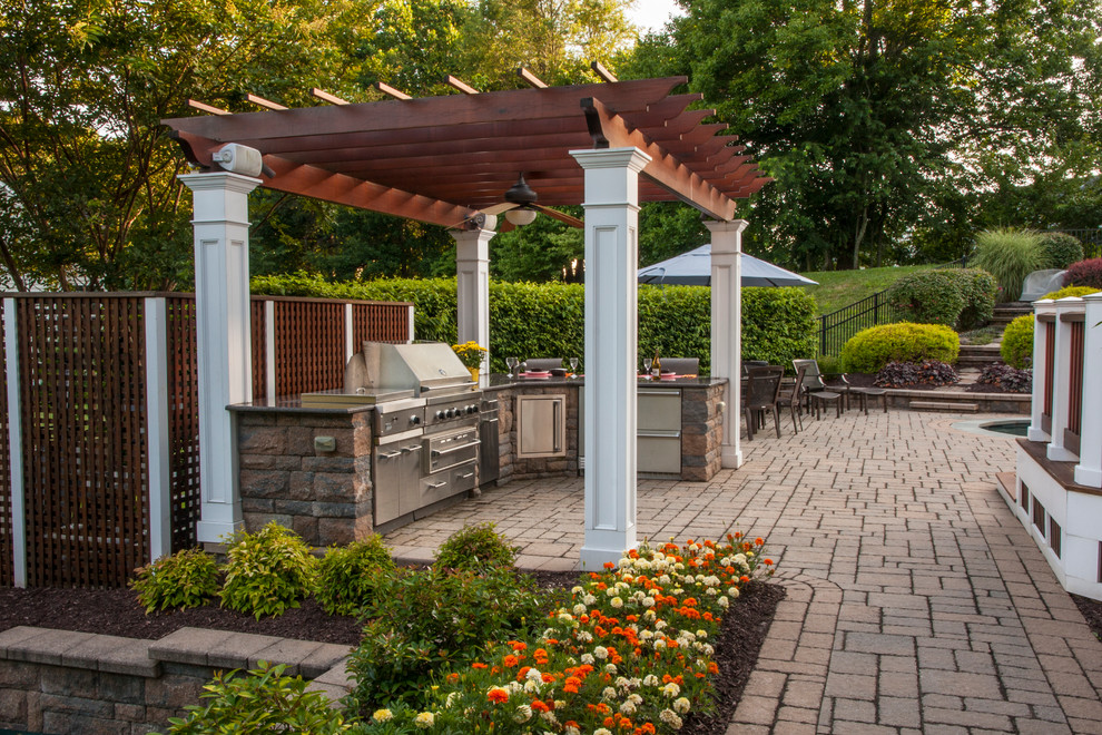 Mid-sized traditional backyard patio in DC Metro with an outdoor kitchen, natural stone pavers and a pergola.
