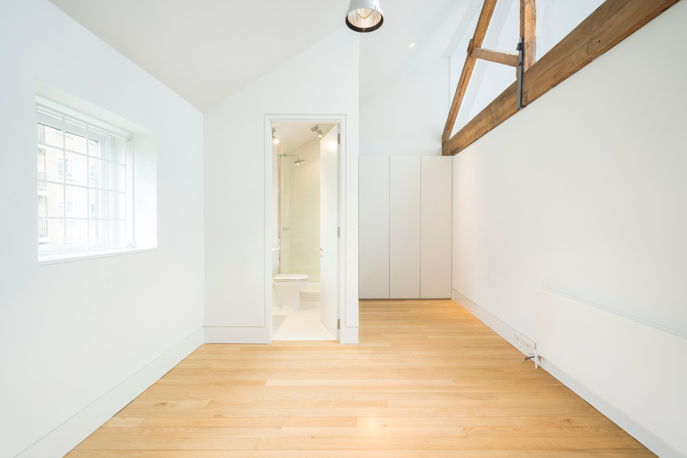 This is an example of a mid-sized industrial guest bedroom in London with white walls and light hardwood floors.