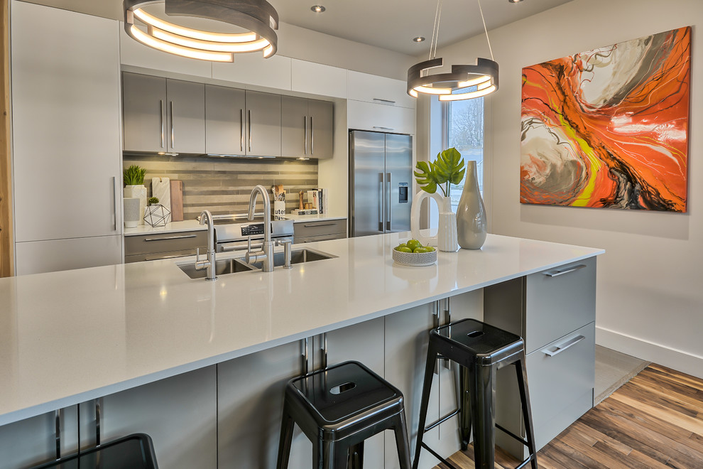 Photo of a mid-sized contemporary galley eat-in kitchen in Montreal with an undermount sink, flat-panel cabinets, grey cabinets, quartz benchtops, grey splashback, ceramic splashback, stainless steel appliances, cork floors, with island and grey floor.