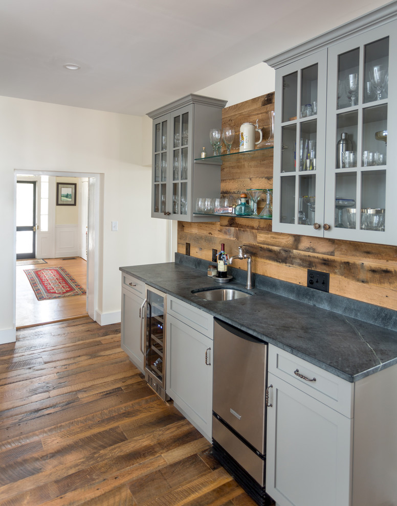 This is an example of a country home bar in Other with glass-front cabinets, soapstone benchtops and timber splashback.