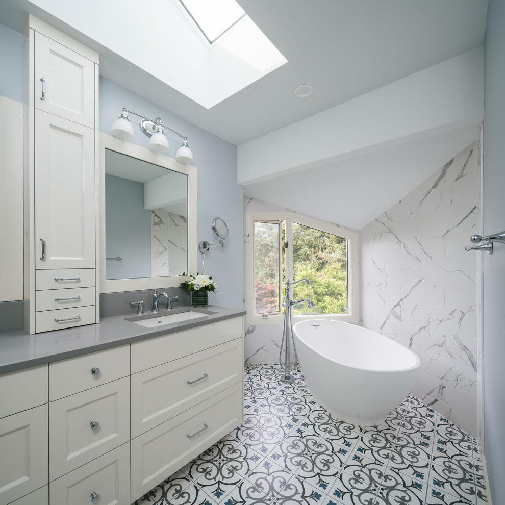 Photo of a transitional bathroom in Portland with recessed-panel cabinets, white cabinets, a freestanding tub, grey walls, an undermount sink, multi-coloured floor and grey benchtops.