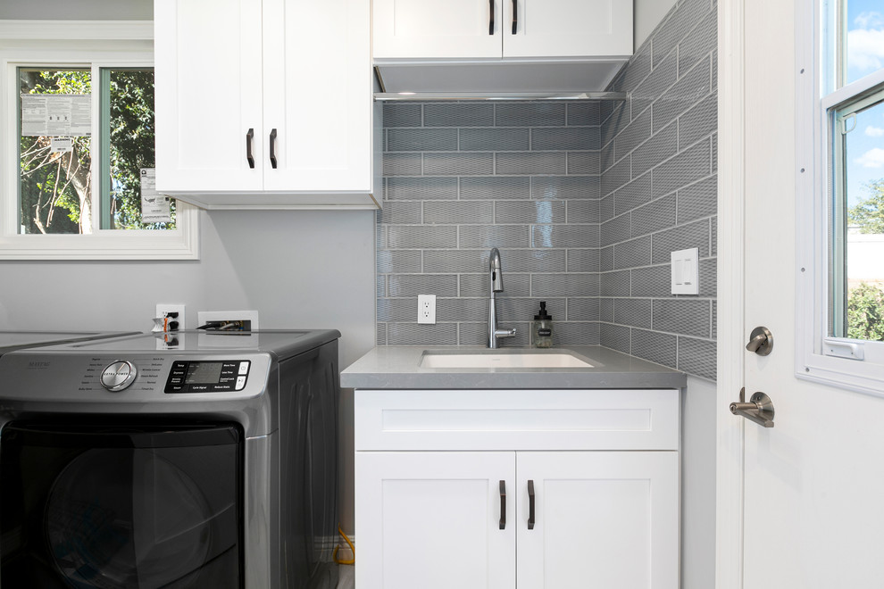 Photo of a transitional dedicated laundry room in Los Angeles with shaker cabinets, white cabinets, quartz benchtops, porcelain floors, a side-by-side washer and dryer, grey floor and grey benchtop.