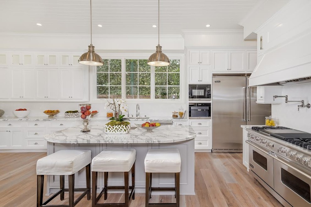 Design ideas for an expansive transitional u-shaped eat-in kitchen in Los Angeles with an undermount sink, white cabinets, white splashback, stainless steel appliances, medium hardwood floors, with island, recessed-panel cabinets, marble benchtops and cement tile splashback.