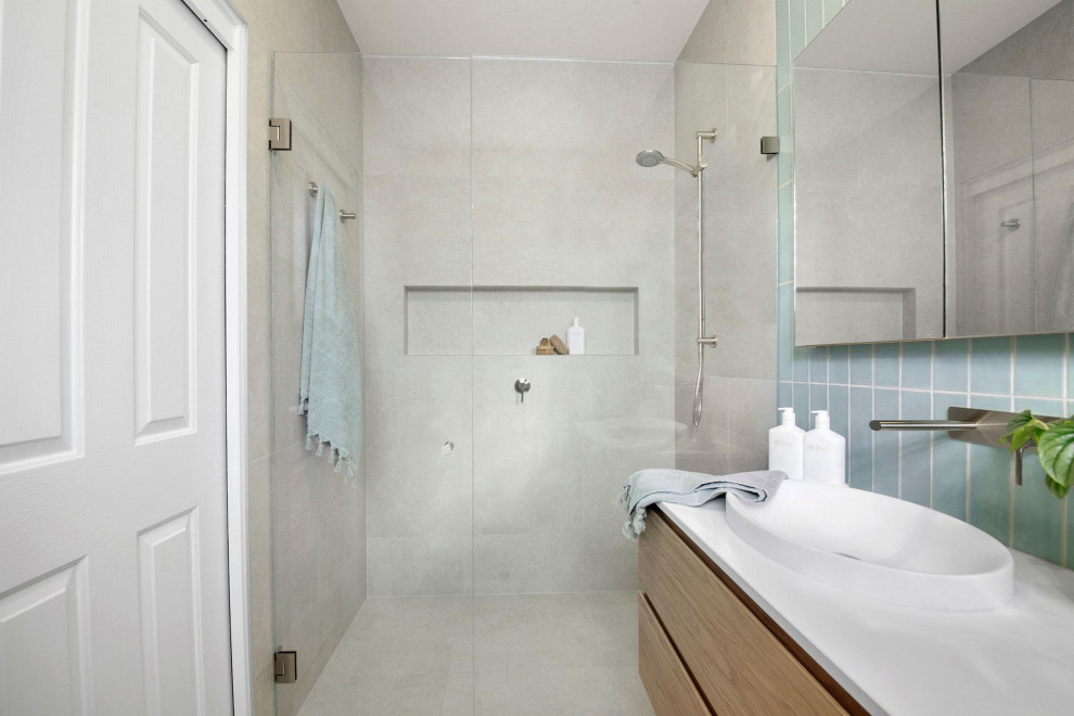 Стильный дизайн: большая главная ванная комната в современном стиле с фасадами островного типа, светлыми деревянными фасадами, отдельно стоящей ванной, угловым душем, унитазом-моноблоком, синей плиткой, плиткой кабанчик, серыми стенами, полом из керамической плитки, накладной раковиной, столешницей из искусственного камня, бежевым полом, душем с распашными дверями, белой столешницей, нишей, тумбой под одну раковину и подвесной тумбой - последний тренд