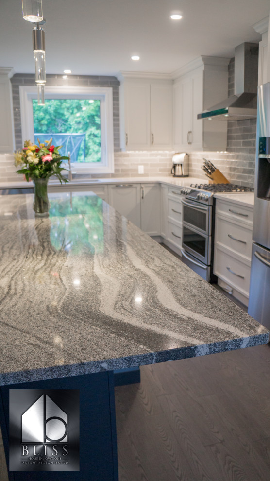 Eat-in kitchen - large transitional l-shaped medium tone wood floor and gray floor eat-in kitchen idea with an undermount sink, recessed-panel cabinets, white cabinets, quartzite countertops, gray backsplash, subway tile backsplash, stainless steel appliances, an island and gray countertops