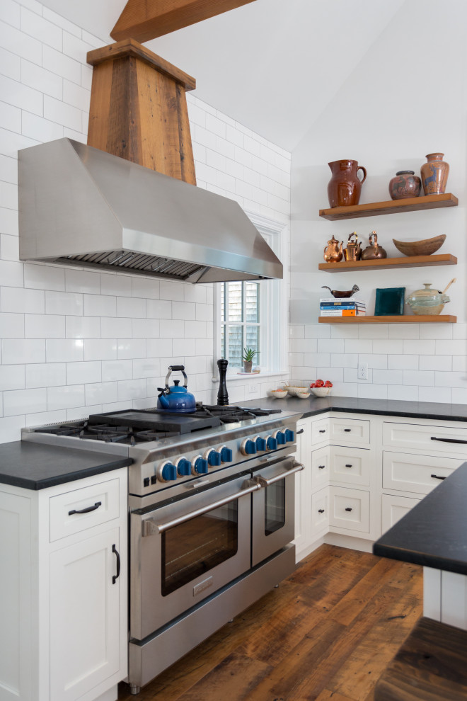 This is an example of a mid-sized country l-shaped kitchen in Boston with an undermount sink, shaker cabinets, white cabinets, quartzite benchtops, white splashback, subway tile splashback, stainless steel appliances, medium hardwood floors, with island, brown floor, black benchtop and exposed beam.