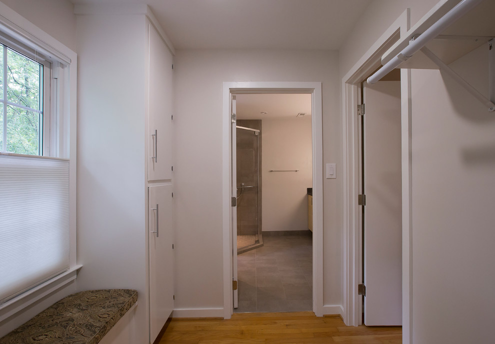 This is an example of a mid-sized contemporary gender-neutral dressing room in Raleigh with flat-panel cabinets, white cabinets, medium hardwood floors and orange floor.