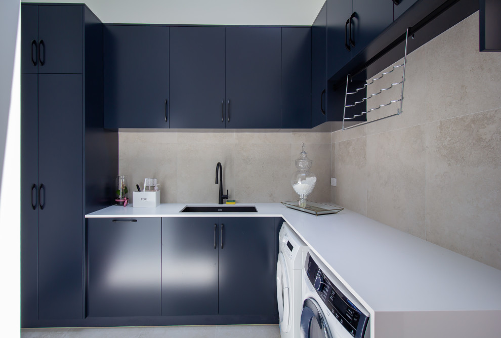 Mid-sized modern l-shaped dedicated laundry room in Sydney with an undermount sink, flat-panel cabinets, black cabinets, quartz benchtops, grey splashback, porcelain splashback, white walls, porcelain floors, a side-by-side washer and dryer, grey floor and white benchtop.