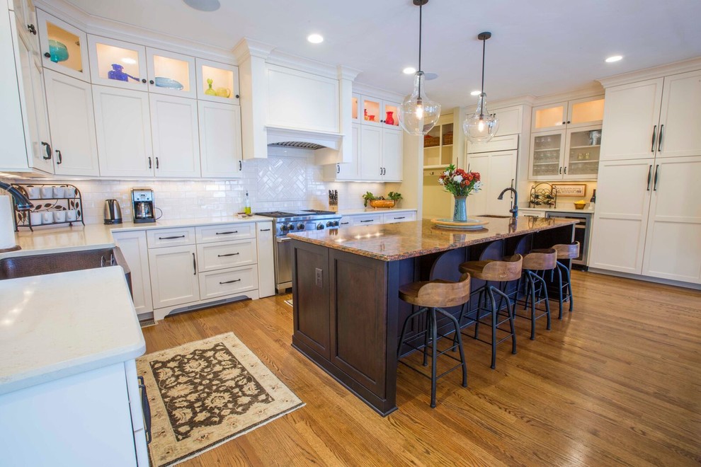 Enclosed kitchen - large transitional l-shaped light wood floor and brown floor enclosed kitchen idea with a farmhouse sink, shaker cabinets, white cabinets, solid surface countertops, white backsplash, porcelain backsplash, stainless steel appliances and an island