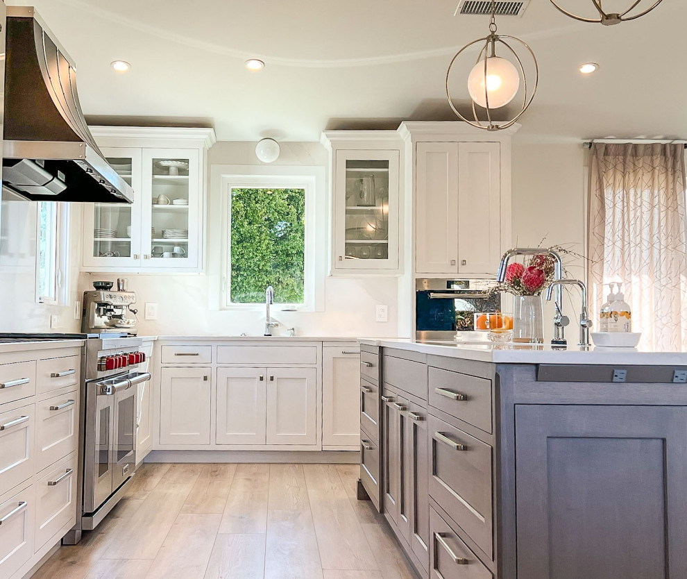 Transitional l-shaped kitchen photo with shaker cabinets, white cabinets, white backsplash, stainless steel appliances, an island and white countertops