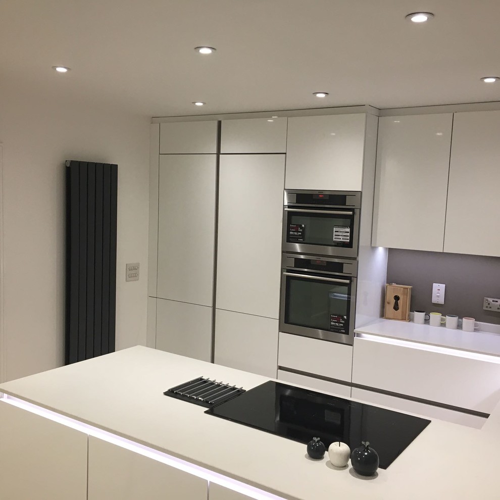 Design ideas for a mid-sized contemporary u-shaped eat-in kitchen in London with an integrated sink, flat-panel cabinets, white cabinets, quartzite benchtops, grey splashback, stainless steel appliances and light hardwood floors.
