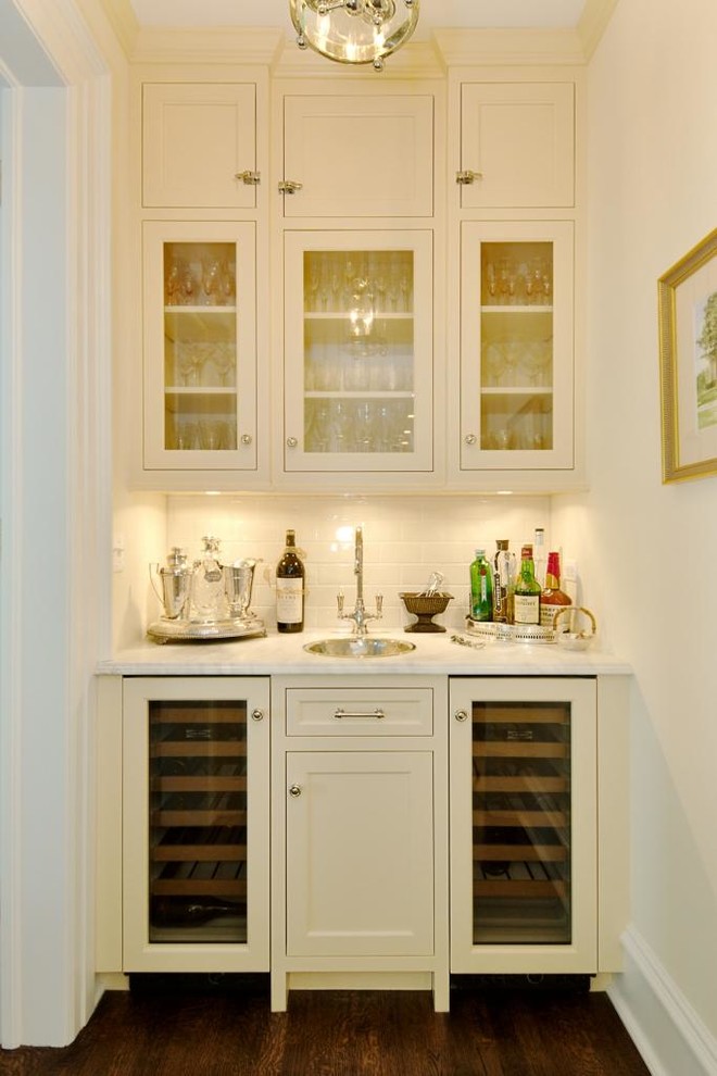 Design ideas for a small traditional single-wall wet bar in Chicago with a drop-in sink, glass-front cabinets, white cabinets, marble benchtops, white splashback, subway tile splashback and dark hardwood floors.