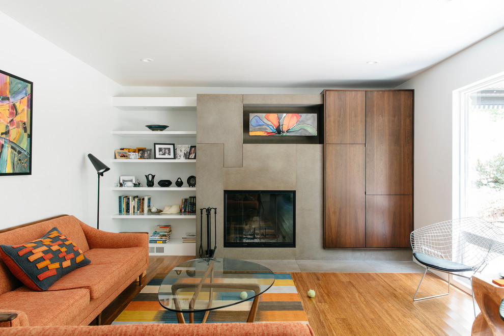 This is an example of a mid-sized midcentury enclosed family room in Omaha with white walls, bamboo floors, a standard fireplace, a concrete fireplace surround and a concealed tv.