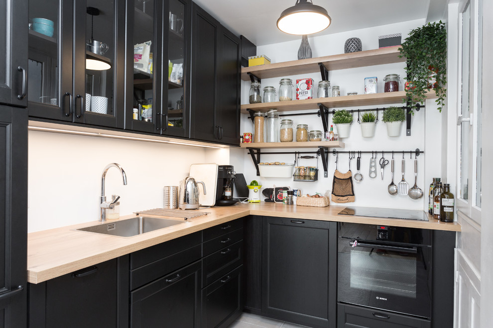 Photo of a scandinavian l-shaped separate kitchen in Paris with a single-bowl sink, recessed-panel cabinets, black cabinets, wood benchtops, white splashback, black appliances, no island, grey floor and beige benchtop.