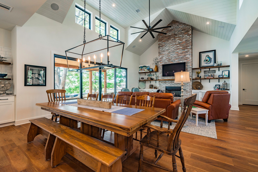 Photo of a mid-sized country open plan dining in Austin with white walls, medium hardwood floors, a standard fireplace, a brick fireplace surround and brown floor.
