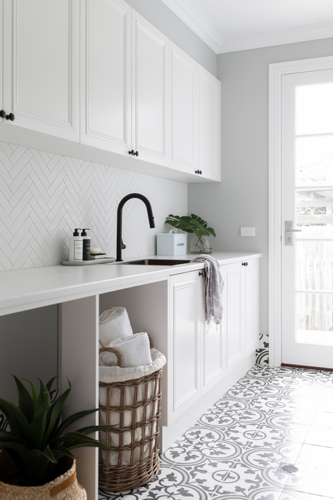 Photo of a mid-sized traditional galley dedicated laundry room in Canberra - Queanbeyan with a single-bowl sink, shaker cabinets, white cabinets, quartz benchtops, white splashback, mosaic tile splashback, grey walls, porcelain floors, a side-by-side washer and dryer, multi-coloured floor and white benchtop.