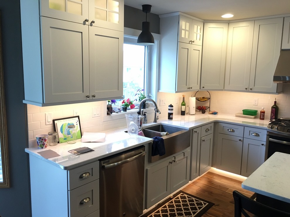 Example of a brown floor kitchen design with a farmhouse sink, white cabinets, white backsplash, stainless steel appliances, an island and white countertops