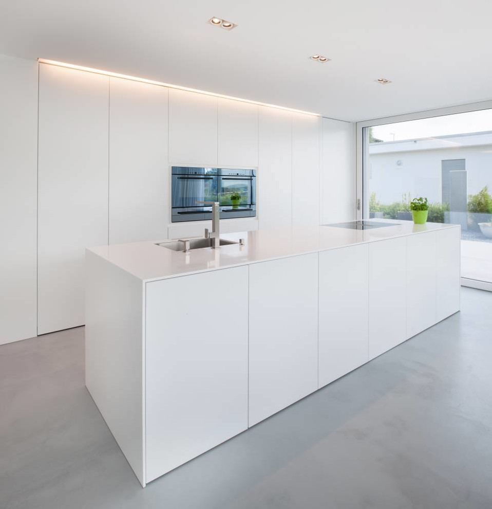Design ideas for an expansive modern open plan kitchen in Nuremberg with solid surface benchtops, white cabinets, concrete floors, an undermount sink, flat-panel cabinets, stainless steel appliances and with island.