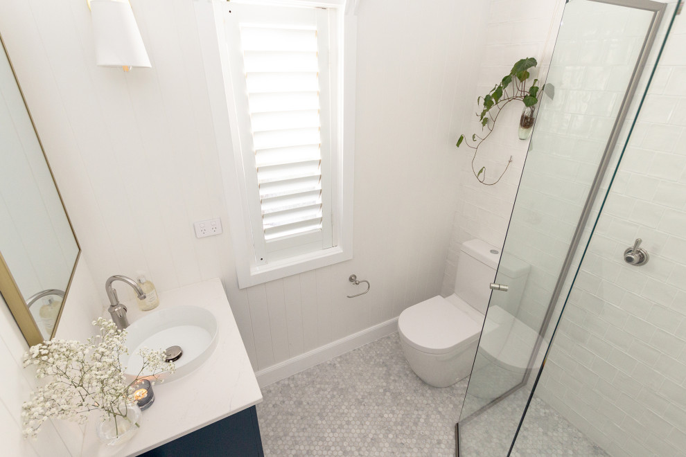 Inspiration for a small 3/4 bathroom in Sydney with shaker cabinets, blue cabinets, a corner shower, a two-piece toilet, white tile, white walls, mosaic tile floors, a drop-in sink, grey floor, a hinged shower door, white benchtops, a single vanity, a floating vanity and panelled walls.
