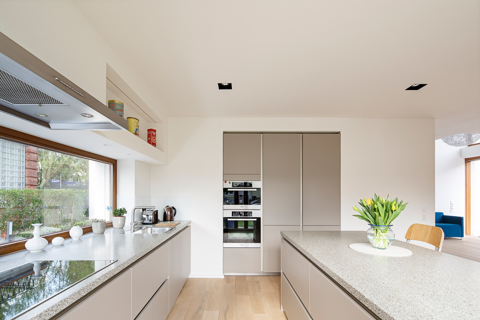 This is an example of a mid-sized modern l-shaped open plan kitchen in Cologne with an undermount sink, flat-panel cabinets, grey cabinets, panelled appliances, light hardwood floors and with island.