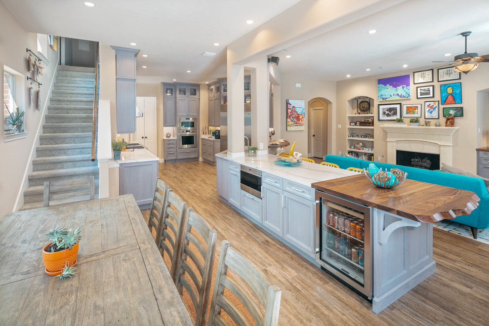 Photo of an expansive transitional open plan kitchen in Houston with recessed-panel cabinets, grey cabinets, quartz benchtops, stainless steel appliances, porcelain floors, with island, brown floor and white benchtop.