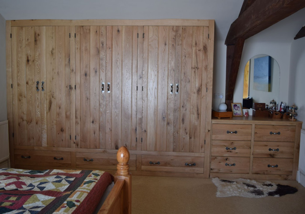 Aménagement d'une grande armoire encastrée classique en bois brun avec un placard à porte affleurante, moquette, un sol beige et poutres apparentes.