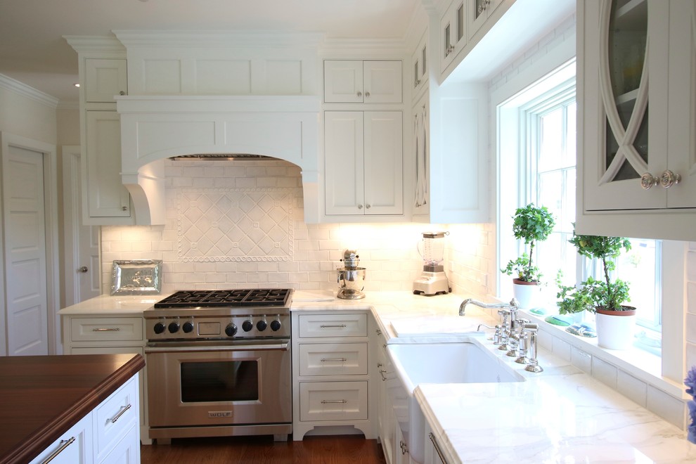 Inspiration for a large beach style u-shaped eat-in kitchen in Boston with a farmhouse sink, beaded inset cabinets, white cabinets, marble benchtops, white splashback, stone tile splashback, white appliances, medium hardwood floors and with island.