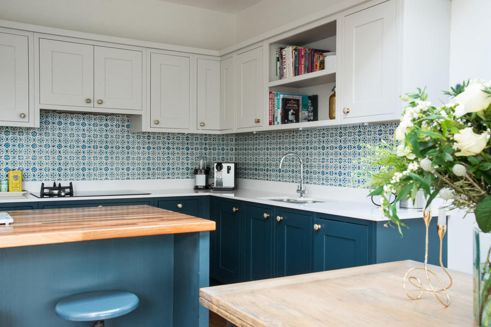 Photo of a mid-sized traditional l-shaped eat-in kitchen in Edinburgh with shaker cabinets, blue cabinets, ceramic splashback, with island, an undermount sink, solid surface benchtops, white splashback and dark hardwood floors.