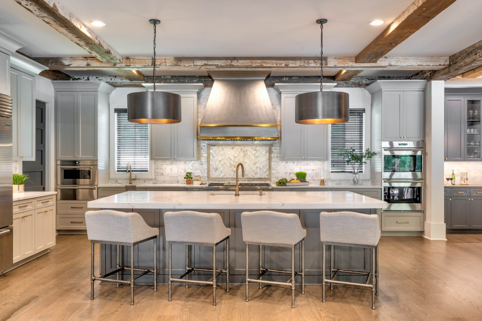 Photo of an expansive transitional l-shaped eat-in kitchen in Atlanta with an undermount sink, shaker cabinets, grey cabinets, quartz benchtops, white splashback, ceramic splashback, stainless steel appliances, medium hardwood floors, with island, brown floor, white benchtop and exposed beam.