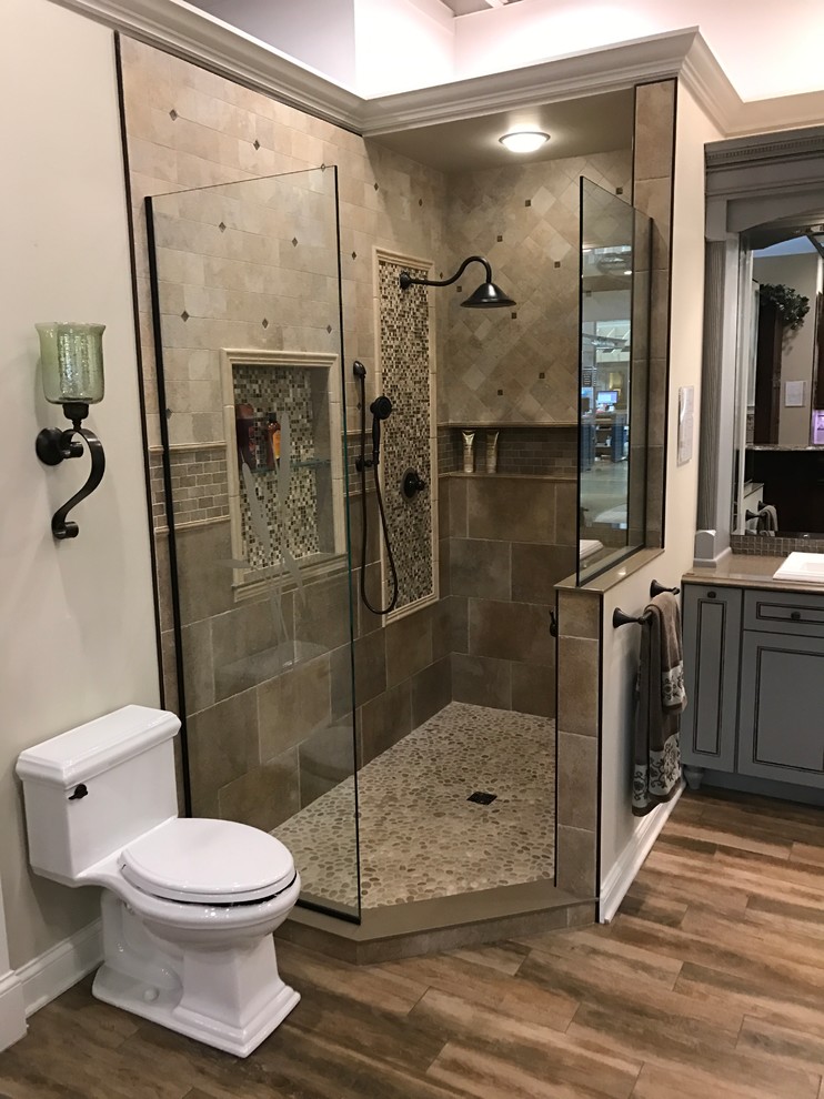 Design ideas for a mid-sized mediterranean master bathroom in Cleveland with beaded inset cabinets, grey cabinets, a freestanding tub, a corner shower, a two-piece toilet, beige tile, ceramic tile, beige walls, medium hardwood floors, a drop-in sink, solid surface benchtops, brown floor and a hinged shower door.