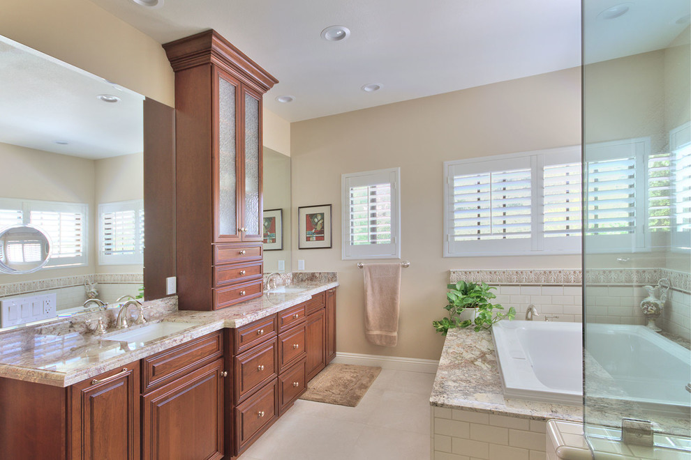 This is an example of a large traditional master bathroom in Los Angeles with recessed-panel cabinets, dark wood cabinets, a drop-in tub, a corner shower, a one-piece toilet, white tile, subway tile, beige walls, an undermount sink and granite benchtops.