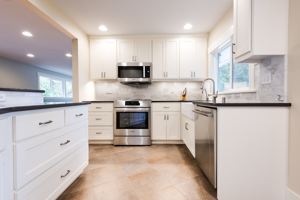 Photo of a mid-sized arts and crafts l-shaped eat-in kitchen in Seattle with a farmhouse sink, shaker cabinets, white cabinets, quartz benchtops, multi-coloured splashback, stone tile splashback, stainless steel appliances and porcelain floors.