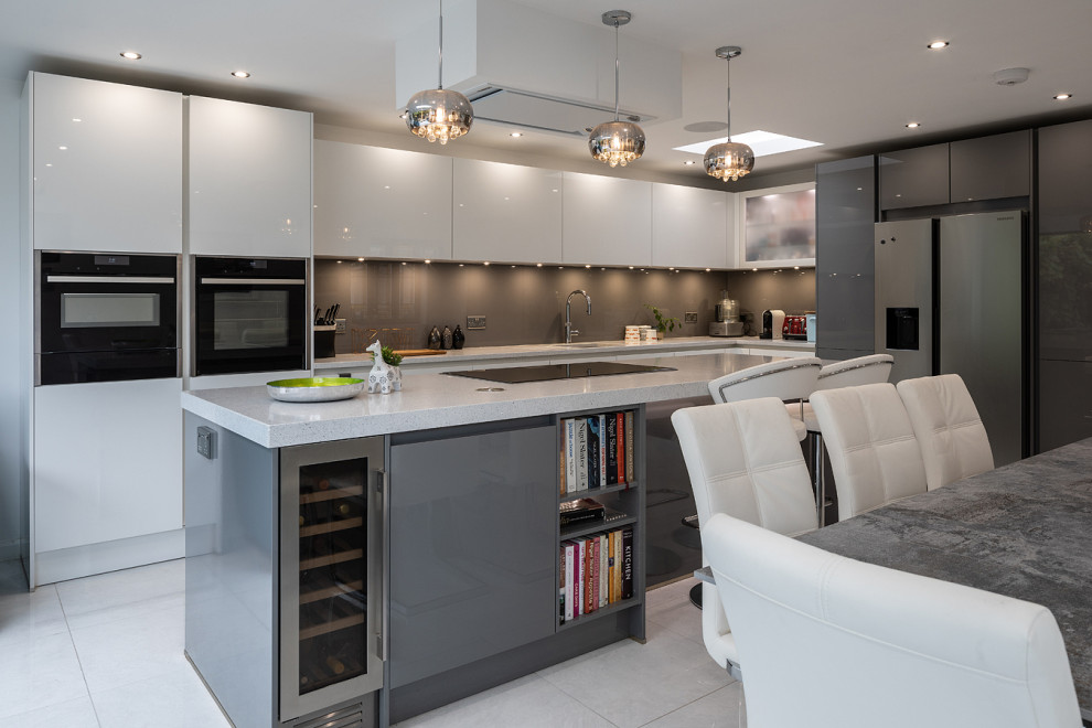 Photo of a large contemporary l-shaped eat-in kitchen in Essex with an undermount sink, flat-panel cabinets, white cabinets, grey splashback, glass sheet splashback, stainless steel appliances, porcelain floors, with island, beige floor and white benchtop.