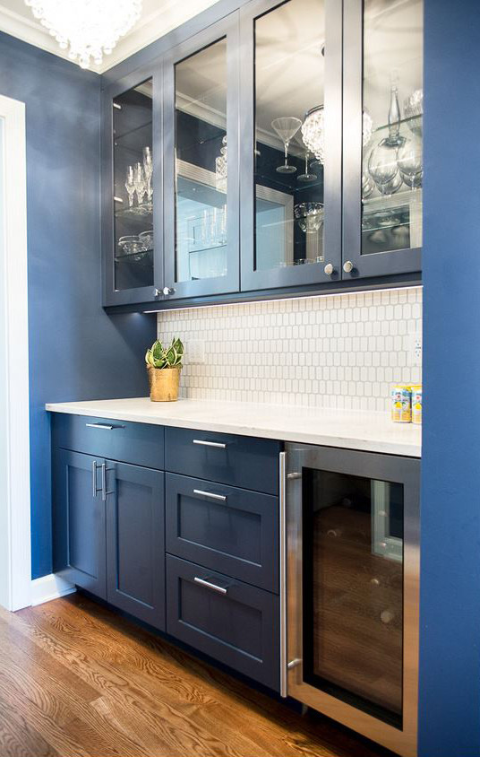 Photo of a mid-sized transitional galley wet bar in Chicago with recessed-panel cabinets, blue cabinets, quartz benchtops, white splashback, porcelain splashback, medium hardwood floors, brown floor and white benchtop.