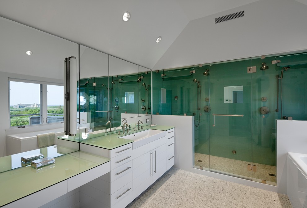 Photo of an expansive arts and crafts master bathroom in New York with flat-panel cabinets, white cabinets, a freestanding tub, an alcove shower, a two-piece toilet, gray tile, mirror tile, white walls, vinyl floors, a trough sink, glass benchtops, white floor and a hinged shower door.