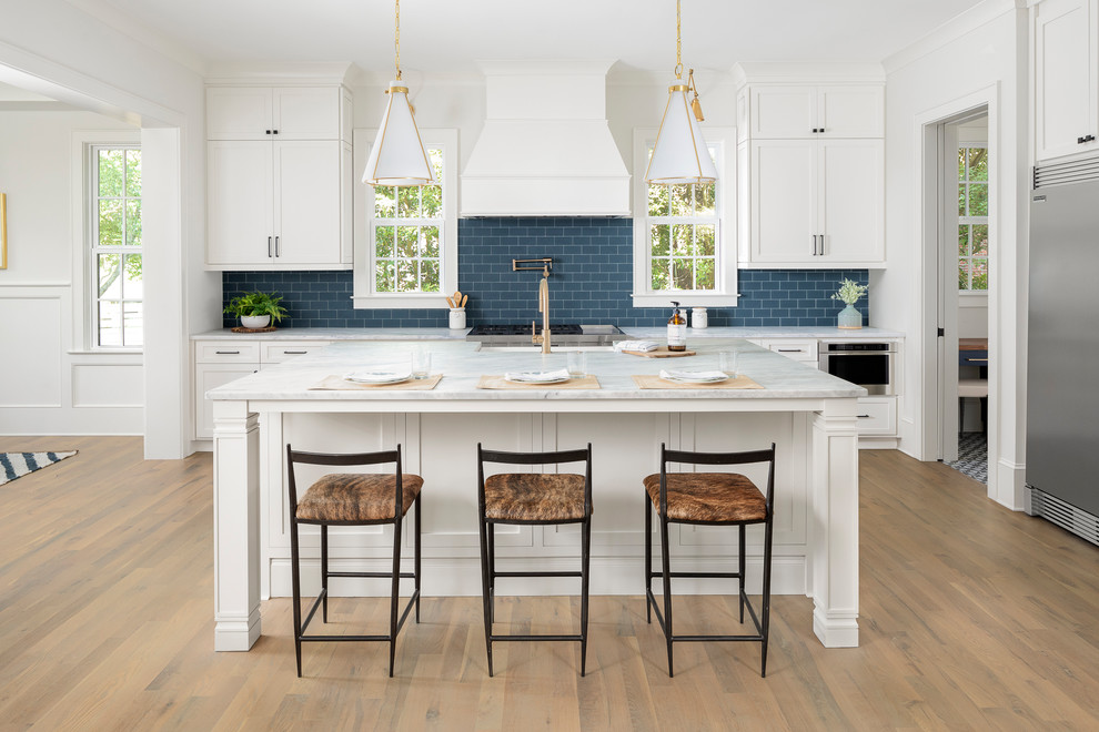 Inspiration for a large transitional light wood floor open concept kitchen remodel in Charlotte with a farmhouse sink, marble countertops, blue backsplash, subway tile backsplash, stainless steel appliances, an island, white countertops, shaker cabinets and white cabinets