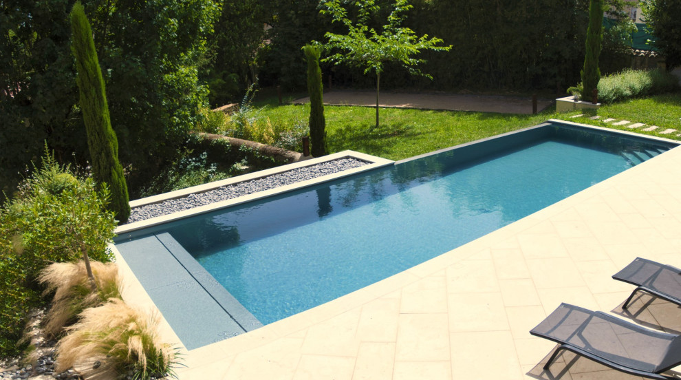 This is an example of a large transitional front yard rectangular infinity pool with natural stone pavers.