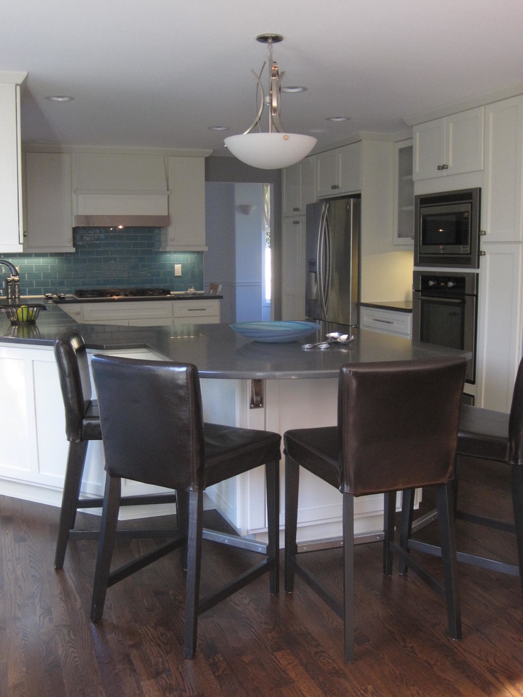 Inspiration for a mid-sized transitional u-shaped dark wood floor home design remodel in Seattle with an undermount sink, shaker cabinets, white cabinets, quartz countertops, blue backsplash, glass tile backsplash, stainless steel appliances and a peninsula