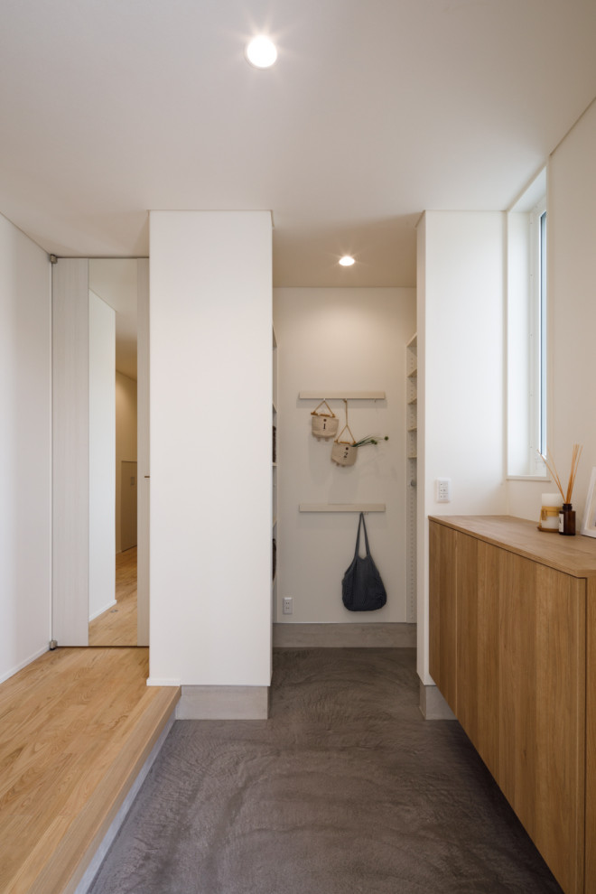 Foto på en minimalistisk hall, med vita väggar, en enkeldörr, mellanmörk trädörr och grått golv